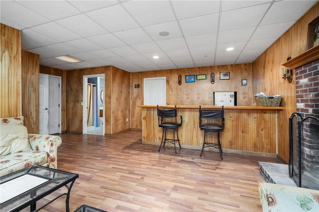 indoor dry bar with light wood-style flooring, wood walls, recessed lighting, a paneled ceiling, and baseboards