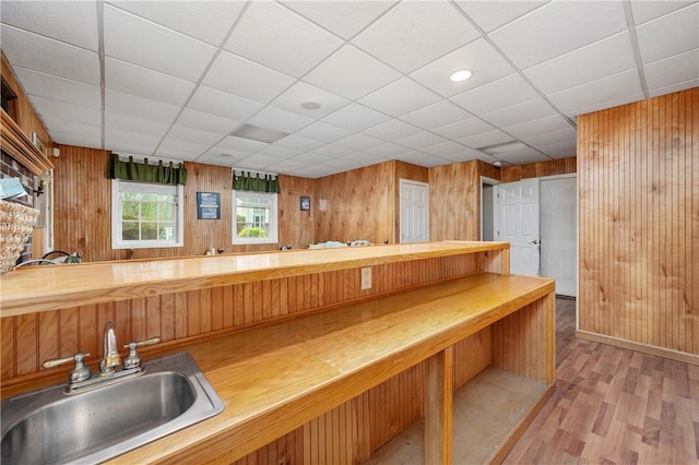 bar with a sink, wood walls, light wood-type flooring, and a drop ceiling