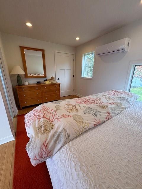 bedroom featuring a wall mounted AC, multiple windows, wood finished floors, recessed lighting, and baseboards