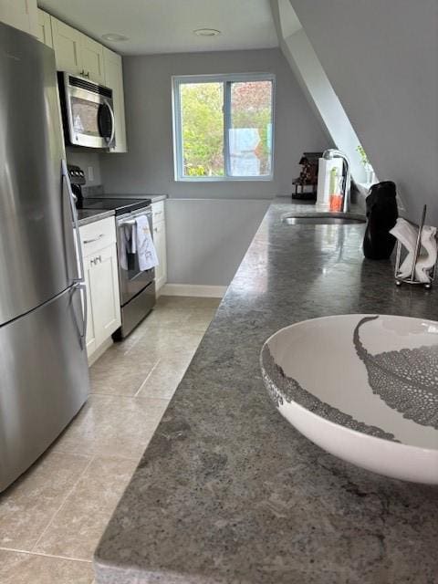 kitchen with appliances with stainless steel finishes, a sink, white cabinets, and baseboards