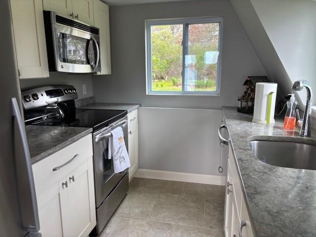 kitchen featuring appliances with stainless steel finishes, a sink, dark stone counters, and baseboards