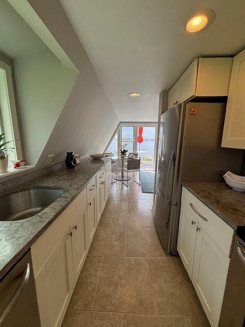 kitchen featuring stainless steel dishwasher, a sink, white cabinets, dark stone countertops, and recessed lighting