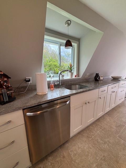 kitchen featuring stainless steel dishwasher, white cabinetry, a sink, decorative light fixtures, and dark stone countertops