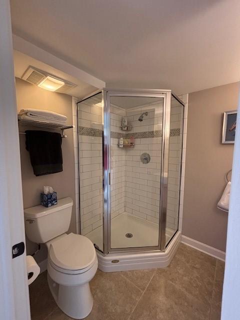 bathroom featuring a shower stall, toilet, tile patterned flooring, and baseboards