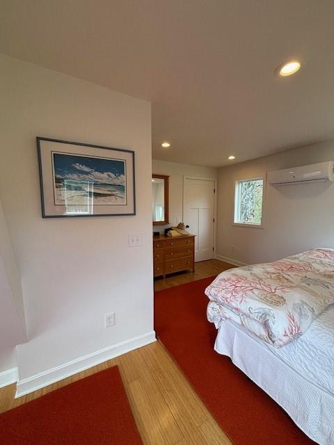 bedroom featuring light wood finished floors, recessed lighting, baseboards, and a wall mounted air conditioner
