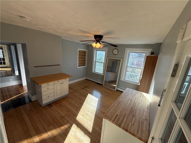 unfurnished dining area with a baseboard radiator, wood-type flooring, a ceiling fan, and baseboards