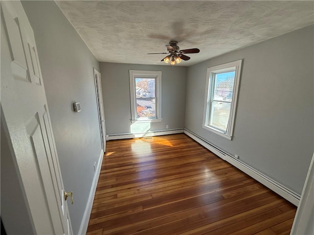 empty room with a baseboard heating unit, dark wood-type flooring, baseboards, plenty of natural light, and a textured ceiling