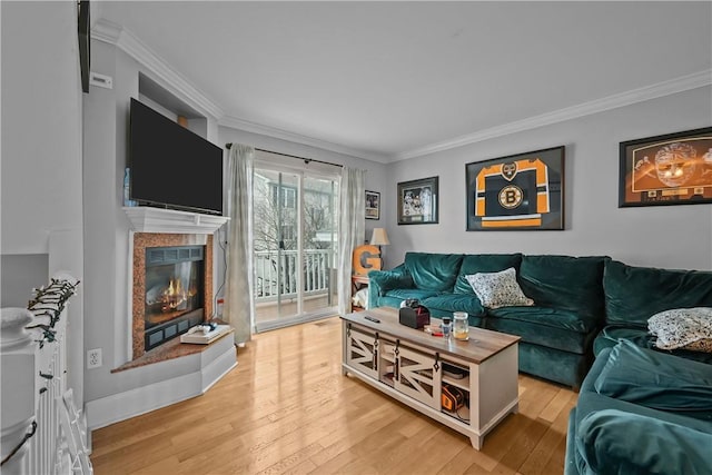 living area featuring crown molding, light wood-style floors, a tile fireplace, and baseboards