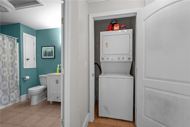 laundry area with stacked washer and clothes dryer, baseboards, and light tile patterned floors