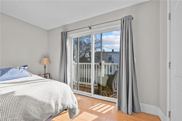 bedroom with access to outside, light wood-type flooring, and baseboards