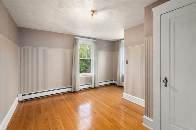 unfurnished room featuring a baseboard radiator, light wood finished floors, wallpapered walls, a wainscoted wall, and baseboards