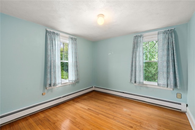 empty room with a baseboard radiator, healthy amount of natural light, hardwood / wood-style flooring, and a textured ceiling