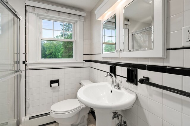 bathroom with baseboard heating, a shower stall, toilet, tile walls, and a sink
