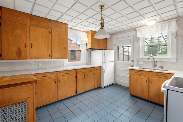 kitchen featuring white appliances, a sink, backsplash, tile patterned floors, and decorative light fixtures