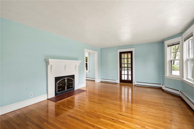 unfurnished living room with a fireplace, light wood-type flooring, baseboard heating, and plenty of natural light
