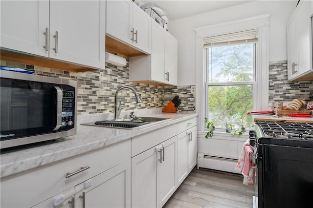 645 Providence St, Woonsocket, RI 02895 - kitchen with a sink, stainless steel microwave, black range with gas stovetop, a baseboard radiator, and white cabinetry