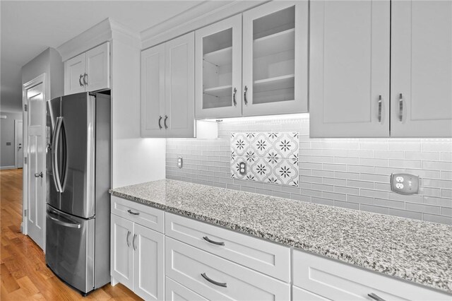 kitchen with freestanding refrigerator, glass insert cabinets, light stone counters, and light wood finished floors