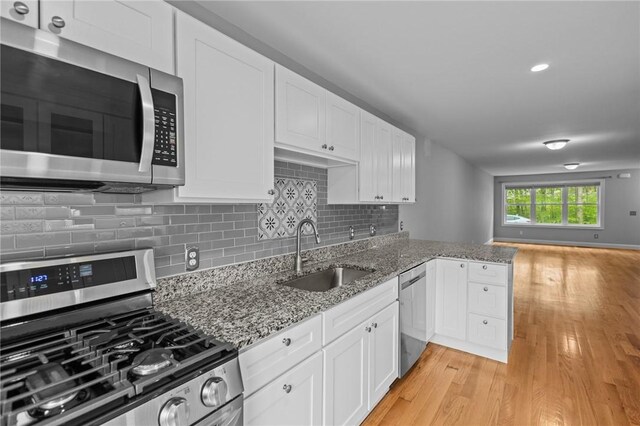 kitchen with stainless steel appliances, a sink, light wood-style floors, and white cabinets