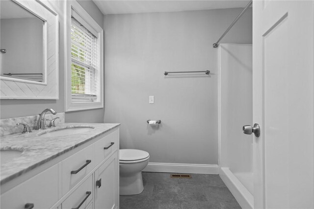 bathroom with toilet, baseboards, vanity, and a shower