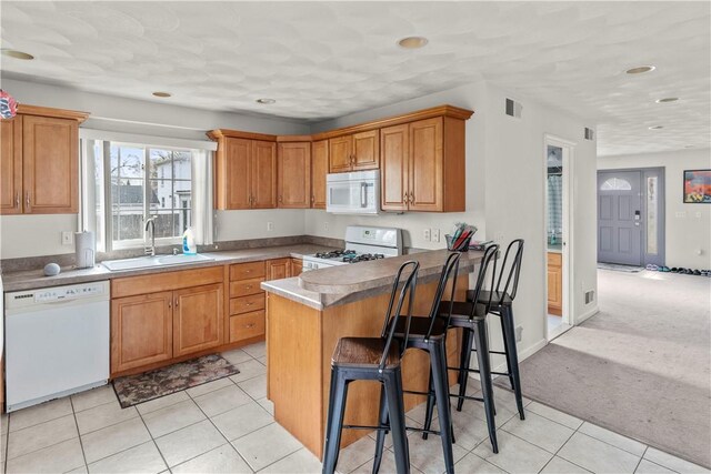 kitchen featuring white appliances, a sink, a kitchen breakfast bar, a peninsula, and light tile patterned floors