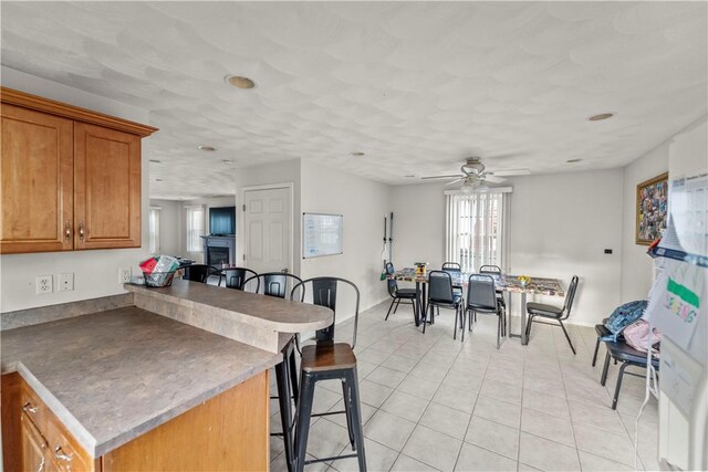 kitchen with a breakfast bar, brown cabinetry, ceiling fan, light tile patterned floors, and a peninsula