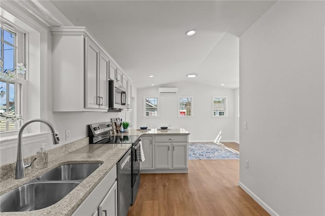 kitchen with stainless steel appliances, a sink, a wall mounted air conditioner, light wood-style floors, and healthy amount of natural light