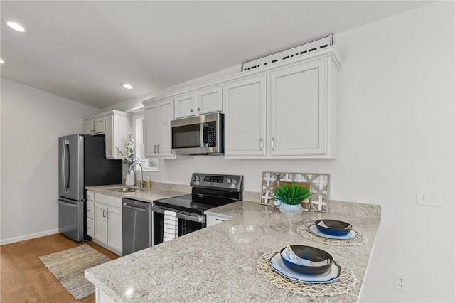 kitchen featuring appliances with stainless steel finishes, a sink, light wood-style floors, recessed lighting, and white cabinetry
