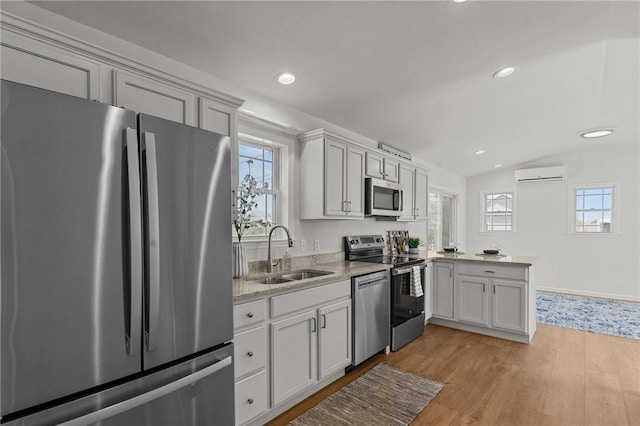kitchen featuring stainless steel appliances, a sink, a wall mounted AC, light wood finished floors, and a peninsula