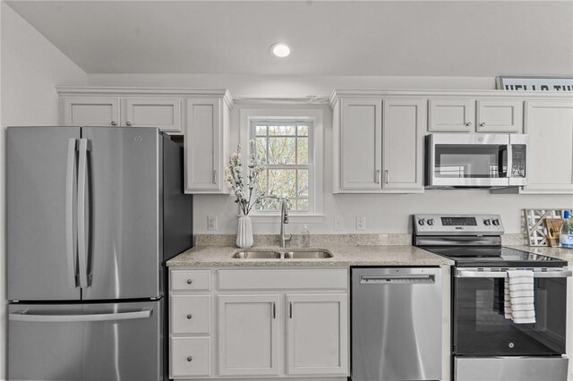 kitchen featuring appliances with stainless steel finishes, a sink, white cabinetry, light stone counters, and recessed lighting