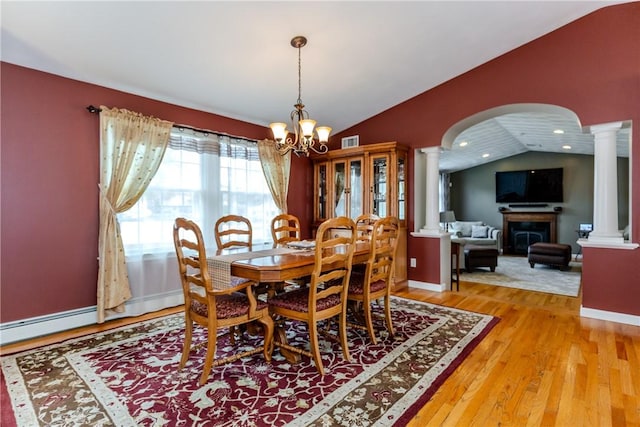 dining area with decorative columns, vaulted ceiling, arched walkways, light wood-style floors, and a chandelier