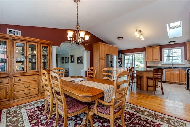 dining area with light wood finished floors, a chandelier, vaulted ceiling, ornate columns, and arched walkways
