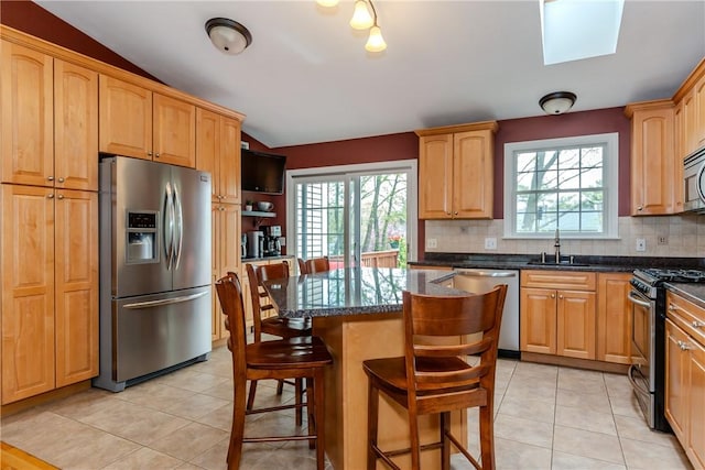 kitchen with appliances with stainless steel finishes, tasteful backsplash, a center island, dark stone countertops, and light tile patterned flooring