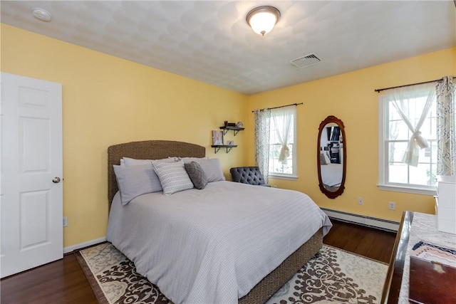 bedroom featuring a baseboard heating unit, wood finished floors, and baseboards
