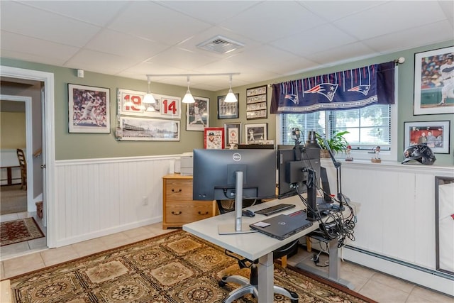 tiled home office with baseboard heating, a paneled ceiling, and a wainscoted wall