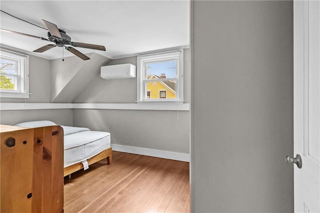 bedroom featuring wood finished floors, a wall mounted AC, baseboards, and ceiling fan
