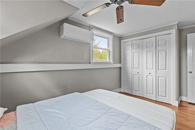 bedroom with a wall unit AC, wood finished floors, ornamental molding, baseboards, and a ceiling fan