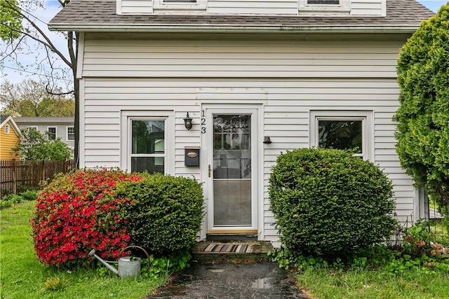 property entrance with a shingled roof and fence