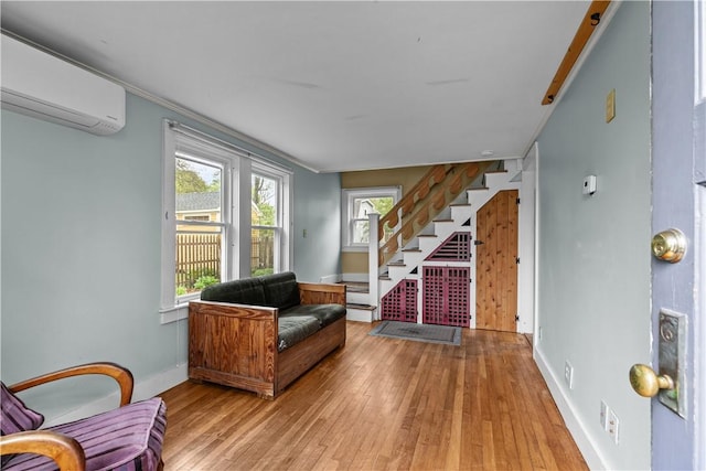 sitting room featuring a wall unit AC, stairs, wood-type flooring, and baseboards
