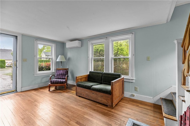 living area featuring an AC wall unit, light wood-style floors, baseboards, and plenty of natural light