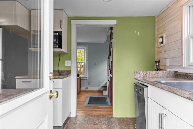 kitchen featuring dishwasher, white cabinets, baseboards, stone counters, and wood walls