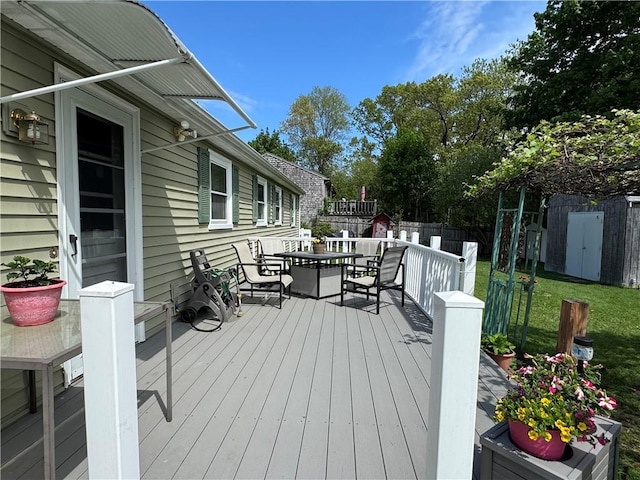 wooden terrace featuring a shed, outdoor dining space, fence, and an outbuilding