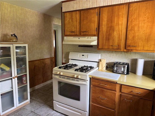 kitchen featuring gas range gas stove, under cabinet range hood, light countertops, light tile patterned floors, and brown cabinetry