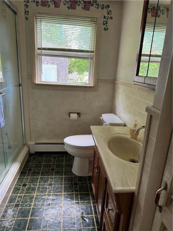 bathroom with tile walls, a baseboard heating unit, a shower stall, vanity, and toilet