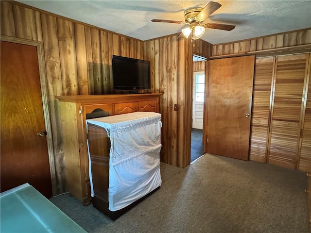 bedroom featuring a textured ceiling, wooden walls, carpet, and ceiling fan