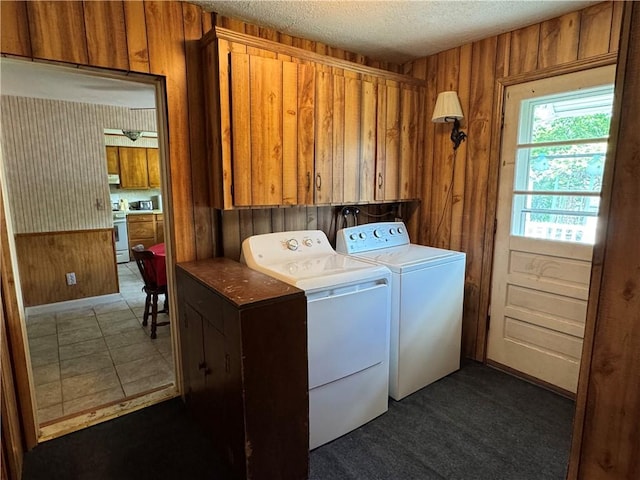 clothes washing area featuring washing machine and dryer, cabinet space, a textured ceiling, and wood walls