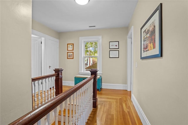 hall with an upstairs landing, baseboards, and light wood finished floors