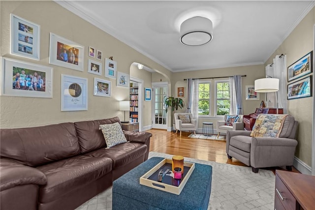 living room with crown molding, light wood finished floors, arched walkways, and baseboards