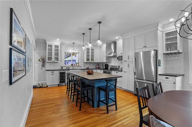 kitchen with stainless steel appliances, beverage cooler, wall chimney range hood, dark countertops, and a breakfast bar area