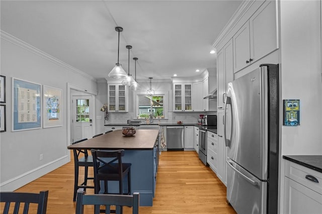 kitchen with stainless steel appliances, dark countertops, a kitchen breakfast bar, crown molding, and glass insert cabinets
