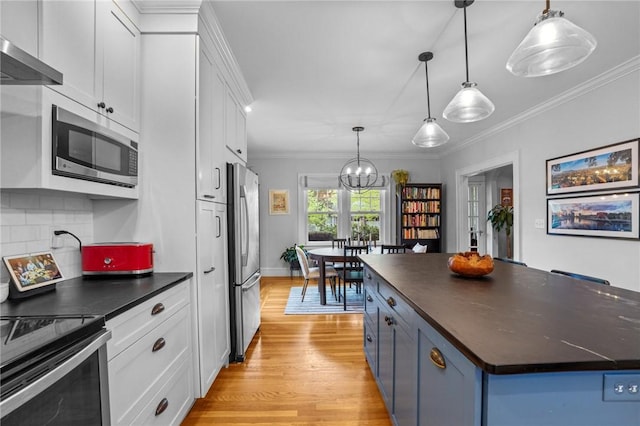 kitchen featuring appliances with stainless steel finishes, dark countertops, white cabinets, decorative backsplash, and ornamental molding